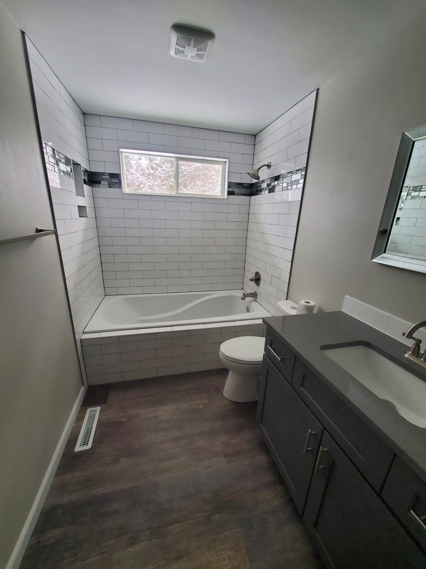 White subway-tile tub surround with a glass mosaic accent stripe by All Things Remodel